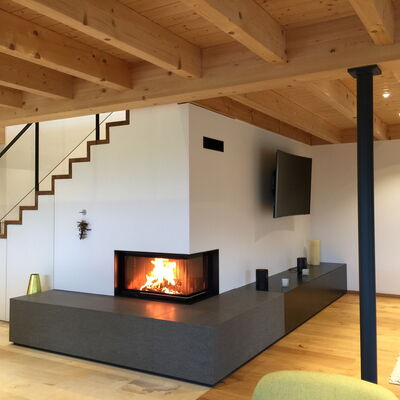 Moderner Eckkamin mit Wärmespeicher, Feuertisch aus dunklem Basalt und Medienboard aus geöltem Rohstahl mit Schubladen.